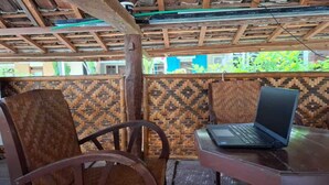 A wooden table with a laptop, two woven chairs, and a patterned wall. - Capital O 94274 Homestay Balimoelih  (Yogyakarta)