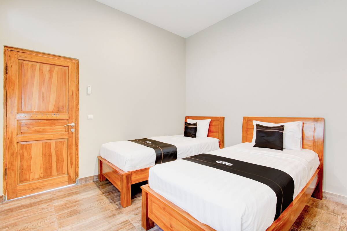 Ein Zimmer mit zwei Holzbetten, jeweils mit einer weiß-schwarzen Bettdecke, einer Holztür und einer hellen Wand.