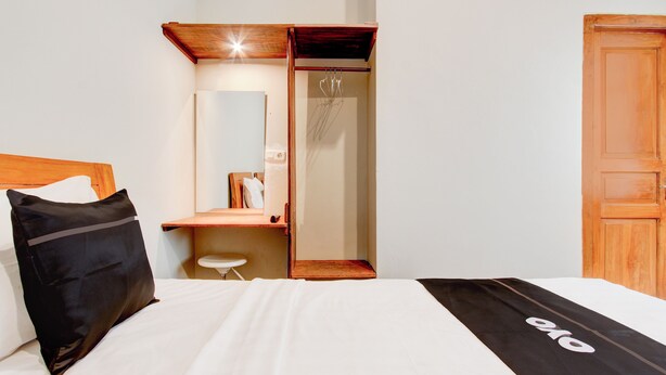 A hotel room with a bed, a wooden headboard, a small stool, a mirror, and a wooden wardrobe. - Capital O 94274 Homestay Balimoelih  (Yogyakarta)