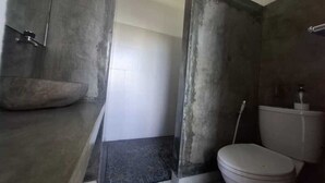 A bathroom with a concrete shower enclosure, a white toilet, and a tiled floor. - Capital O 94274 Homestay Balimoelih  (Yogyakarta)