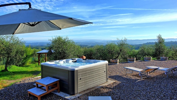 Un jacuzzi con vistas a colinas ondulantes, rodeado por un patio de grava con sillas reclinables y una pérgola que ofrece sombra.