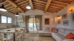 Amplia sala de estar con un sofá beige grande, una mesa de comedor preparada para cuatro comensales y una cocina con encimera blanca y lámparas colgantes.