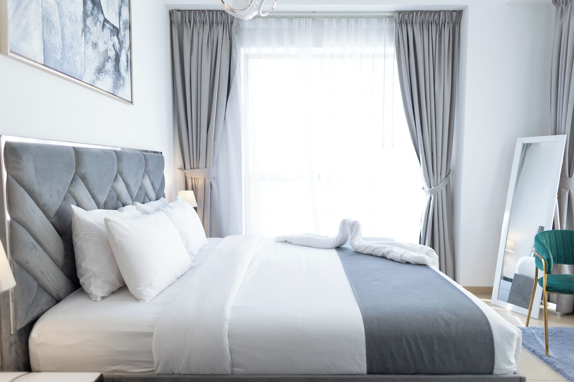 Ein modernes Hotelzimmer mit einem großen Bett, grauen Vorhängen, einem Nachttisch und einem Spiegel.