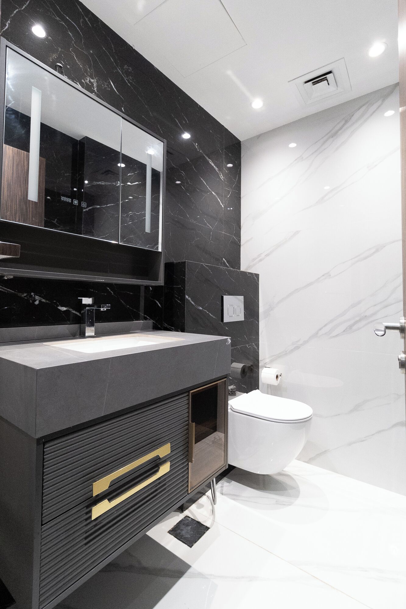 A modern bathroom with a black vanity, a mirror, a toilet, and marble walls.