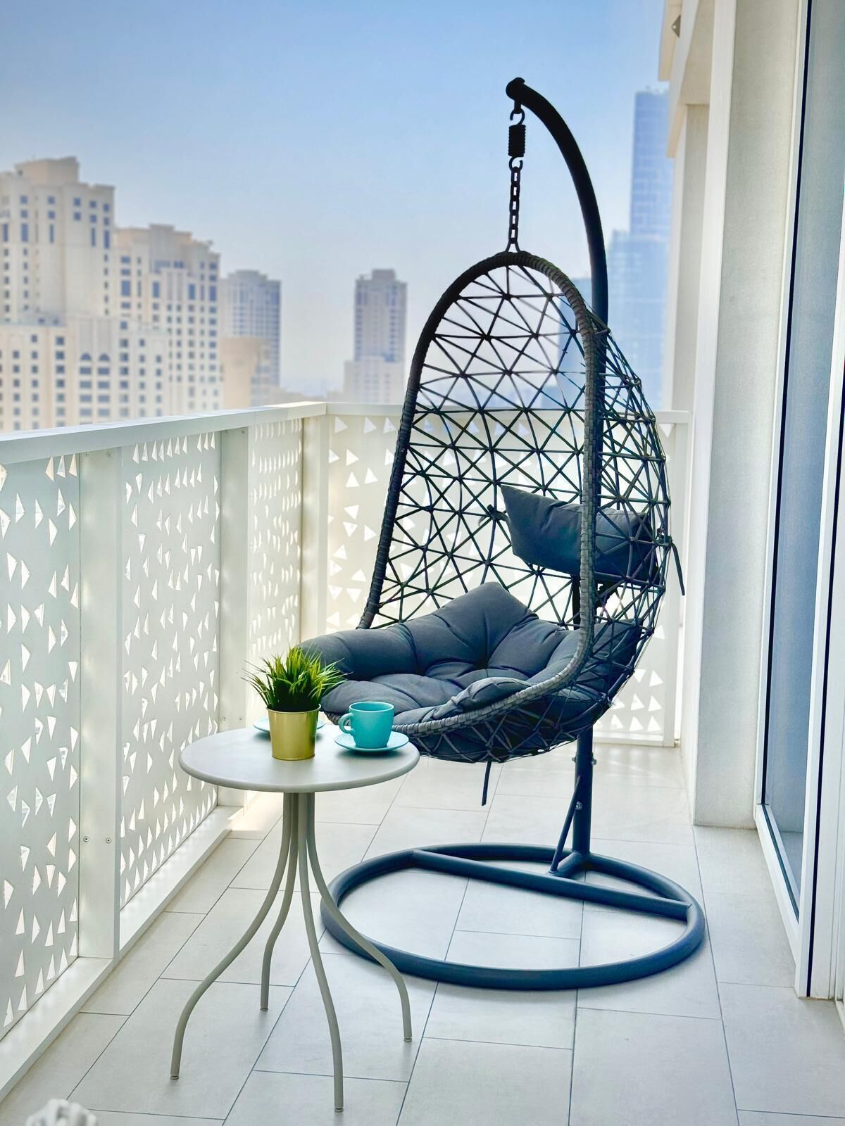 Een balkon met een hangstoel, een kleine tafel en een plant in een pot.