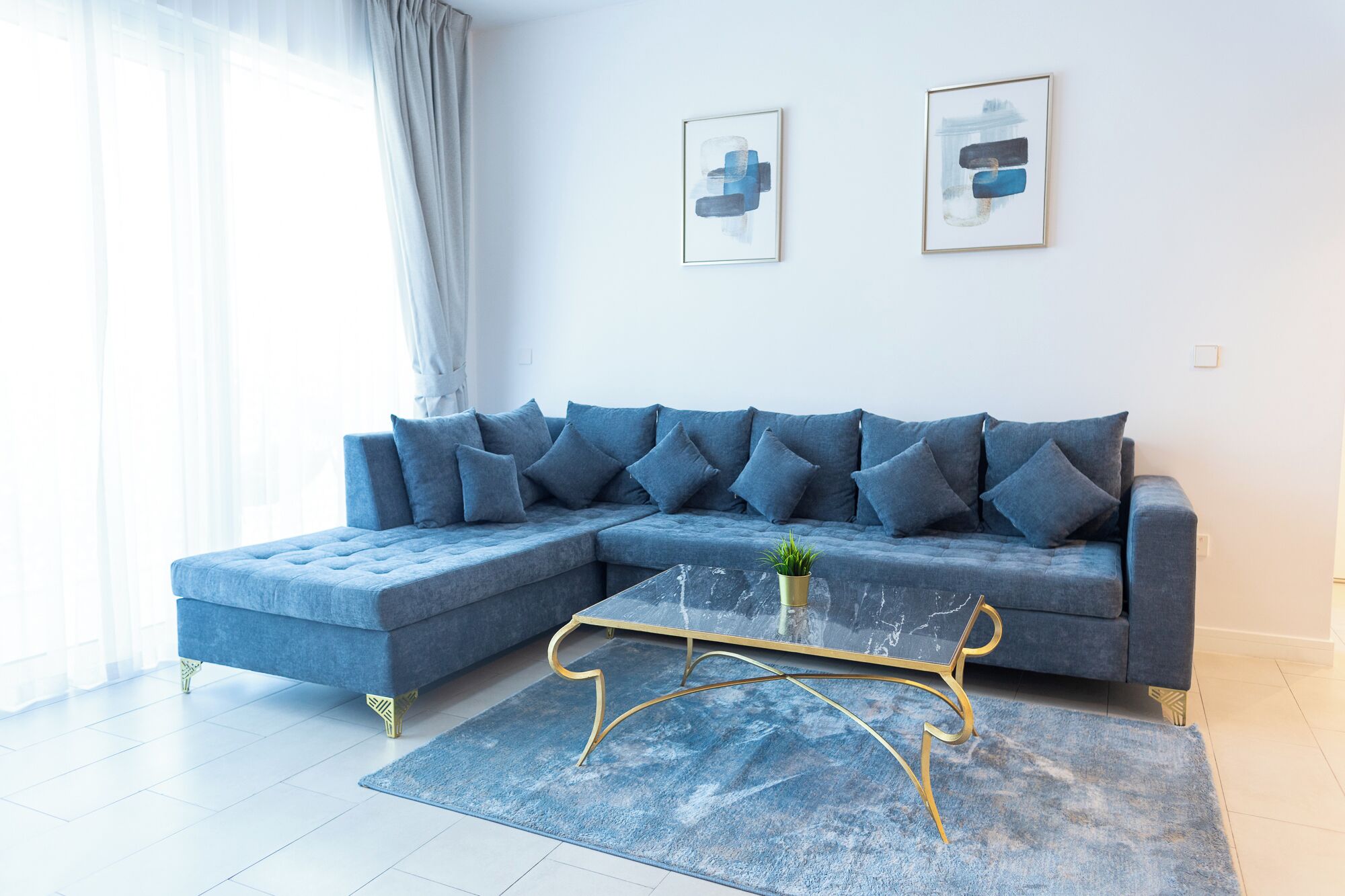 A modern living room with a sectional sofa, a glass coffee table, and two abstract paintings on the wall.
