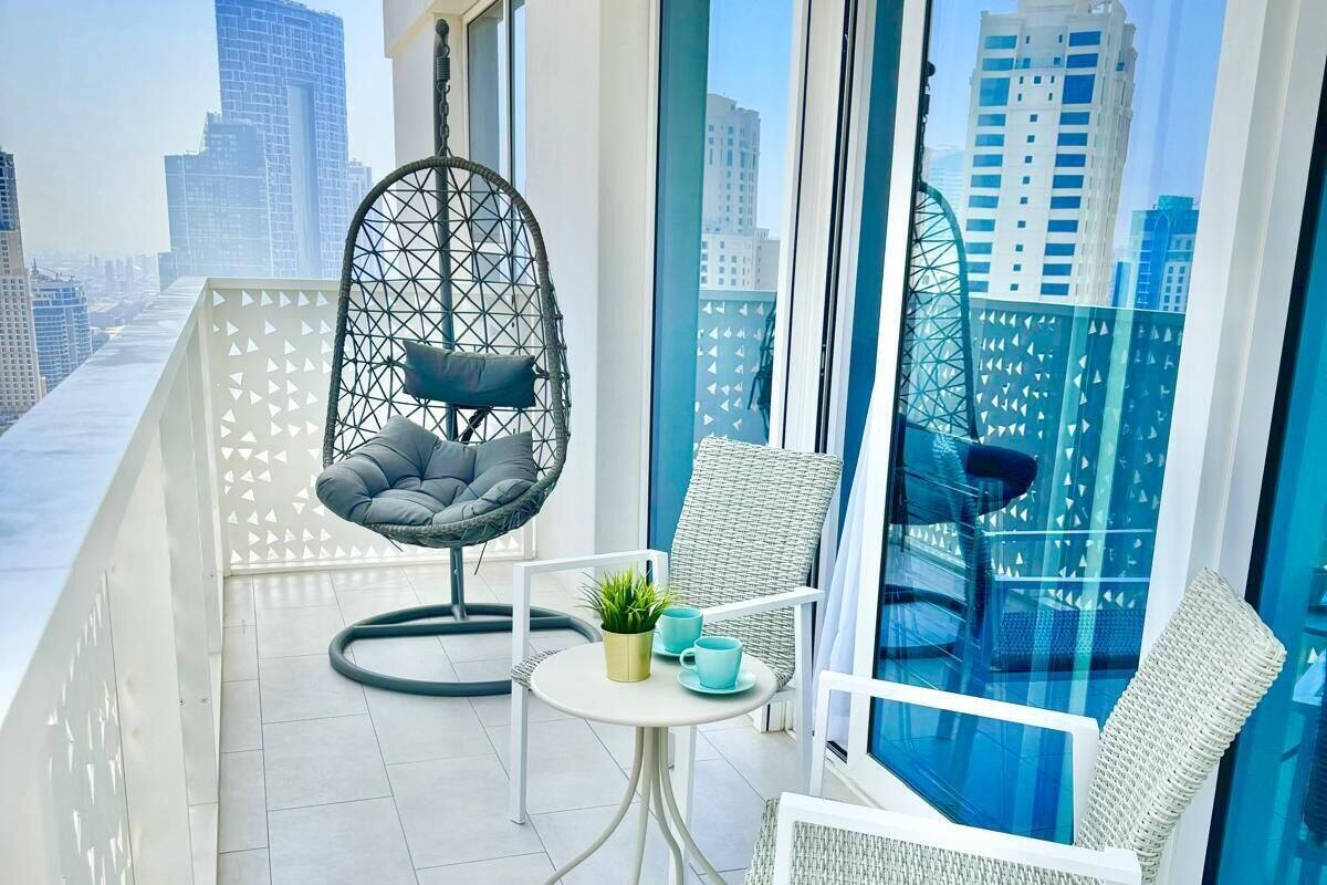 A balcony with a hanging chair, a small table with a plant, and a white chair.