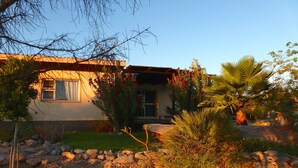 Une maison avec un toit en pente, un porche à l’avant et un jardin agrémenté de rochers et de plantes.