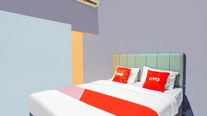 Hotelkamer met een bed, twee rode kussens met de tekst 'OYO', een wit-rode dekbedovertrek en een groen hoofdeinde.