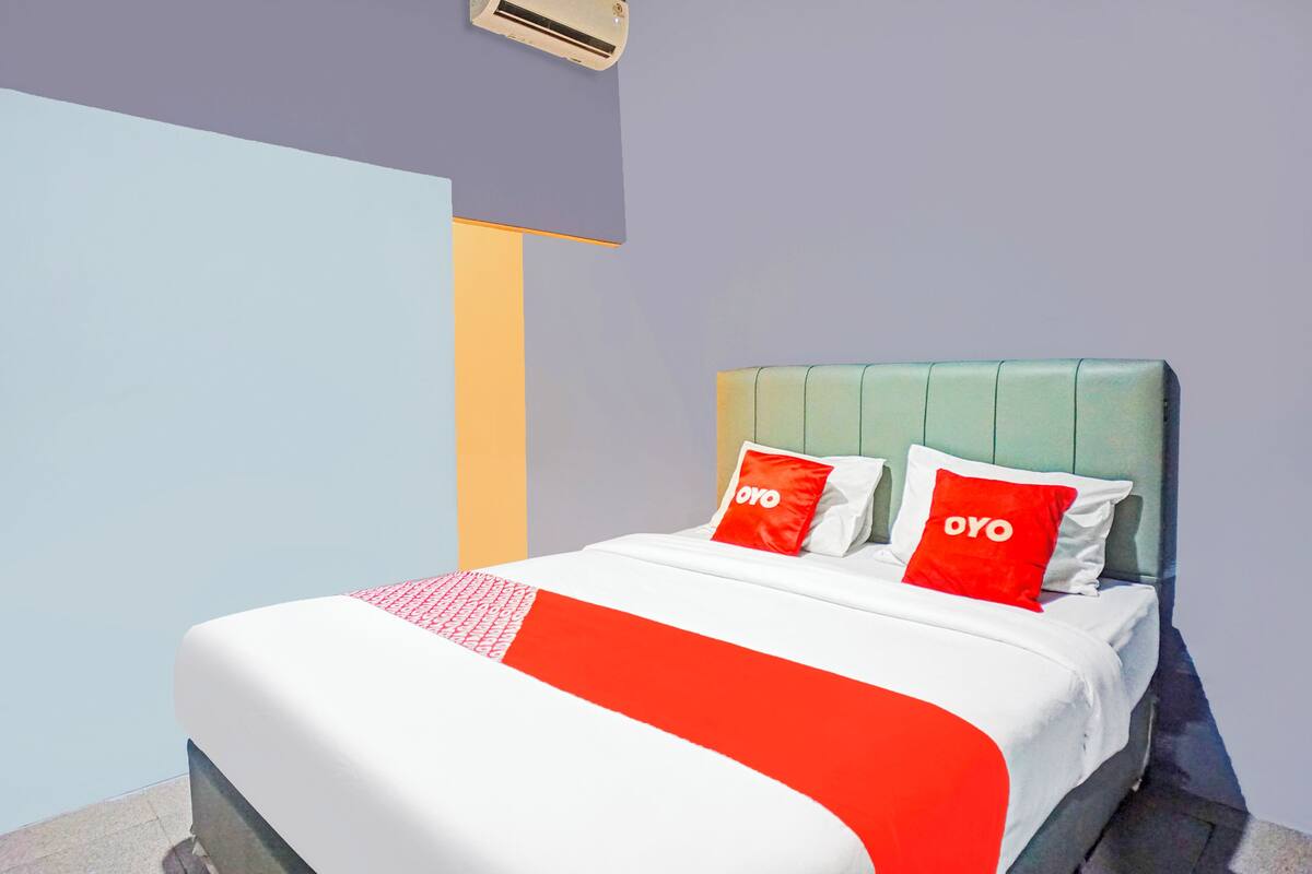 A hotel room with a bed, two red pillows with "OYO" text, a white and red bedspread, and a green headboard.