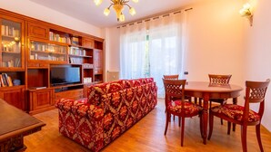 A living room with a sofa, a TV, wooden cabinets, and a dining table with chairs. - Spring Apartment by Wonderful Italy (Como)