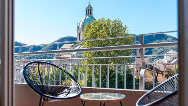 A balcony with two chairs and a small table, overlooking a cityscape with a prominent church dome and surrounding buildings. - Spring Apartment by Wonderful Italy (Como)