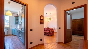 A hallway with a kitchen on the left, a dining area with a patterned sofa, and a wooden door on the right. - Spring Apartment by Wonderful Italy (Como)