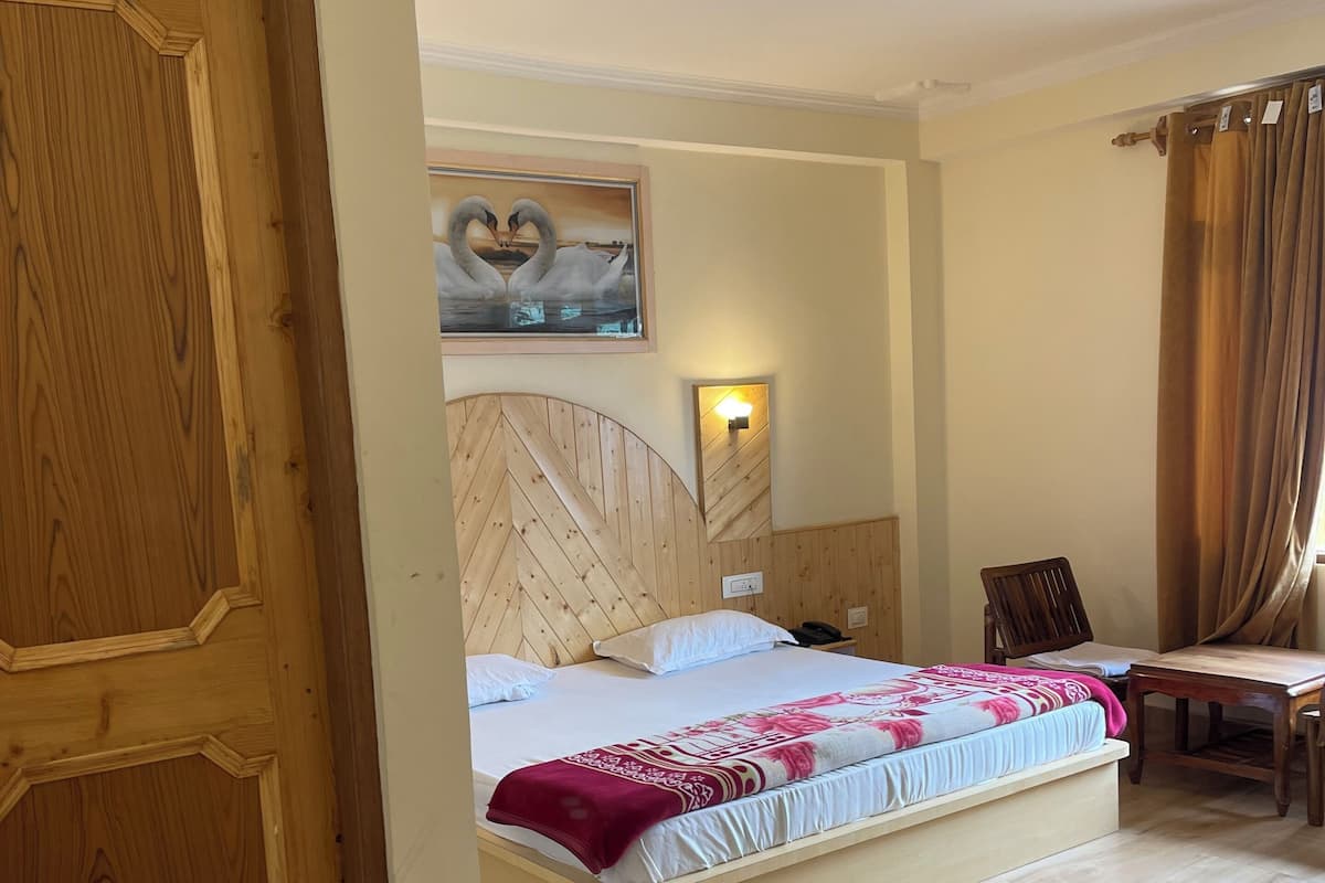 A hotel room with a wooden bed, a desk, a chair, and a painting of swans on the wall.