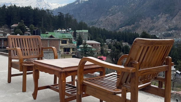 A wooden table and chairs set on a concrete surface with a mountain view in the background. - Shubham Cottage (Manali)