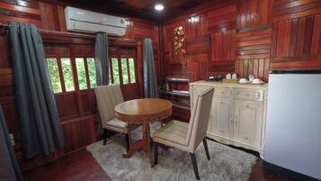 A wooden-paneled room with a dining table, chairs, a white refrigerator, and a window with curtains.