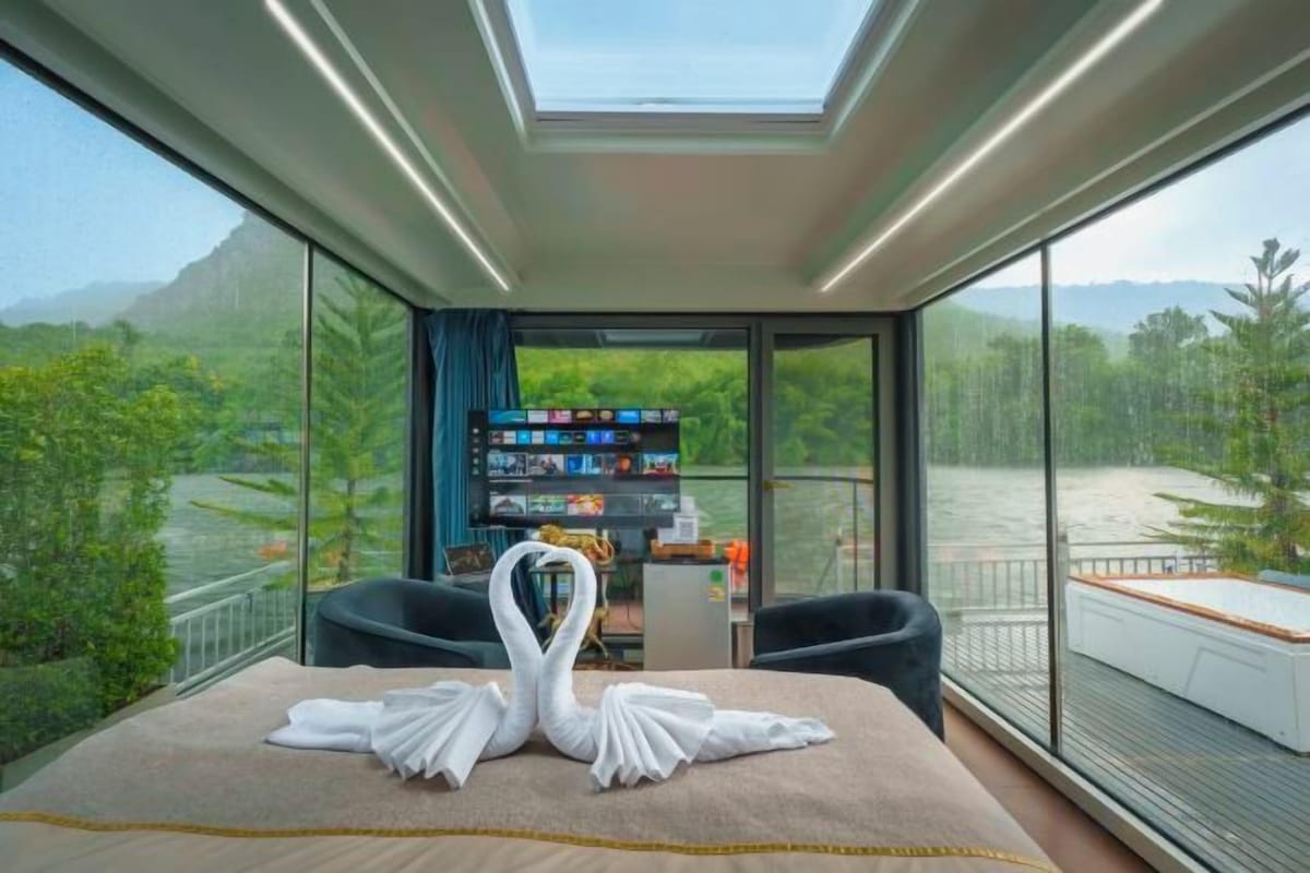 A modern room with a bed, a desk, and a large window overlooking a river.