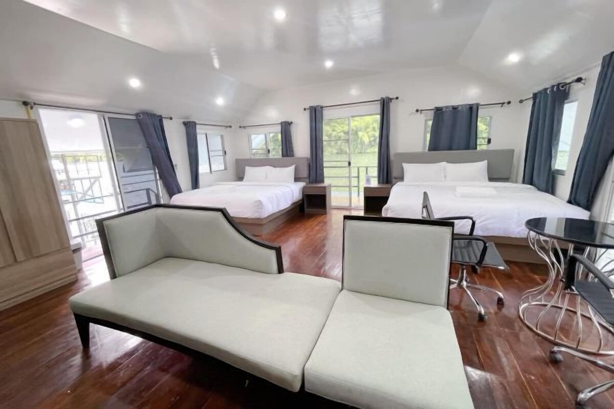 A hotel room with two beds, a sofa, a dining table, and a balcony.