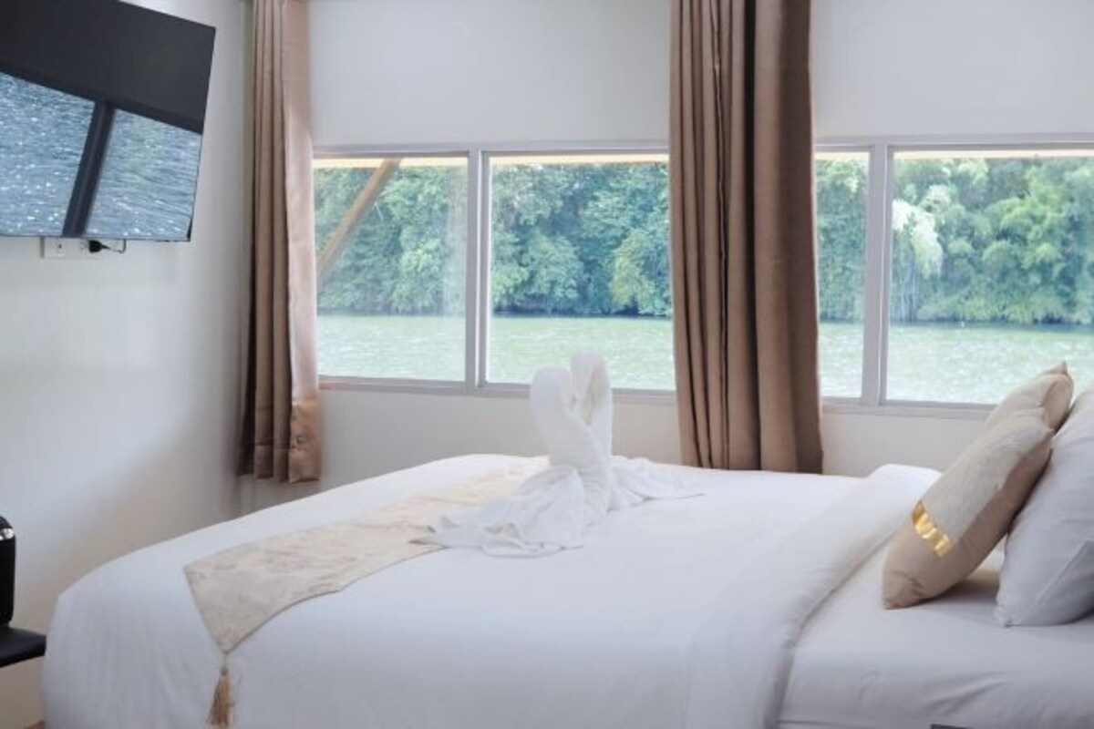 A hotel room with a bed, a TV mounted on the wall, and a window with a view of a body of water and greenery.