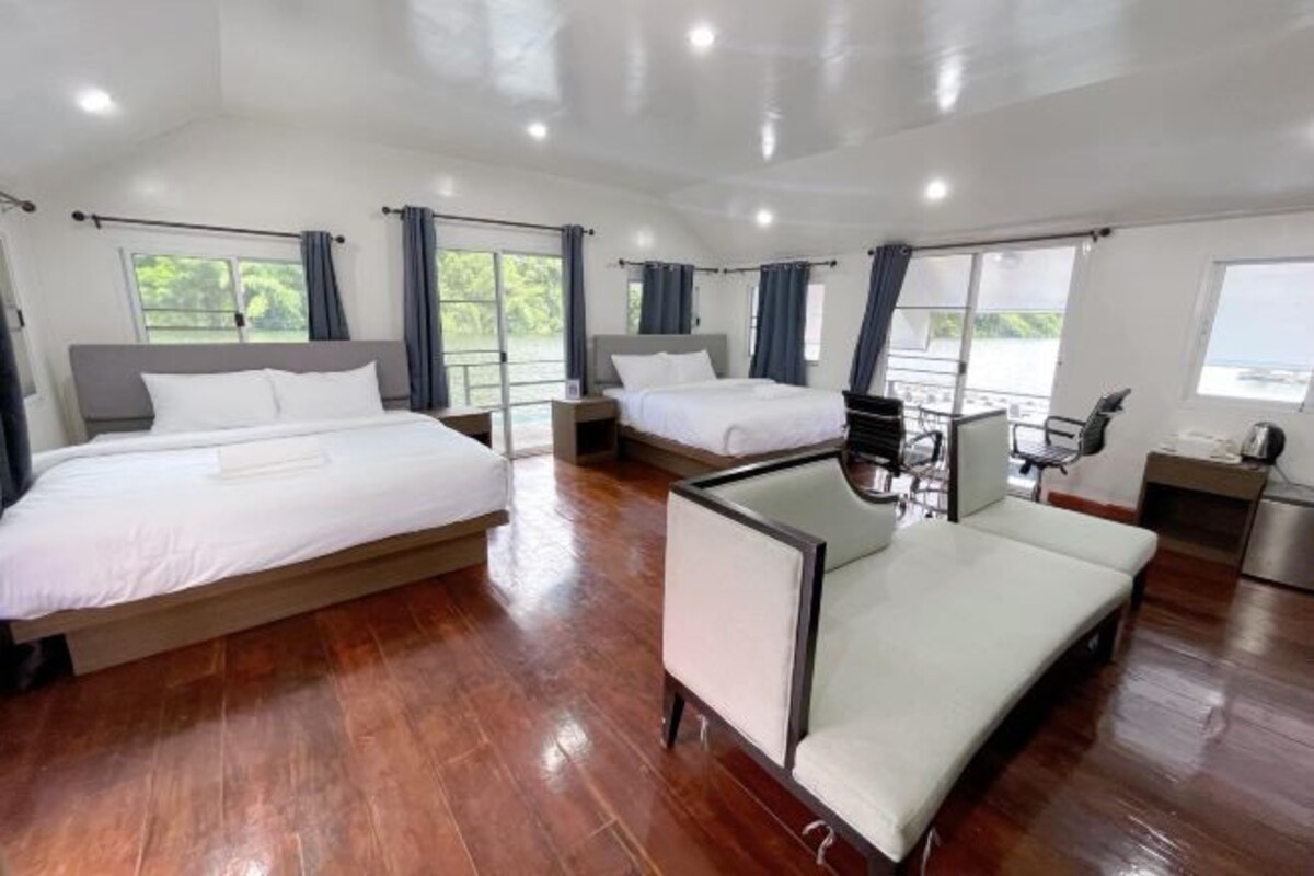 A hotel room with two beds, a sofa, a desk, and a view of the outdoors.