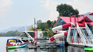 Un parque acuático con un tobogán rojo y blanco, un bote pequeño y un edificio de techo rojo.