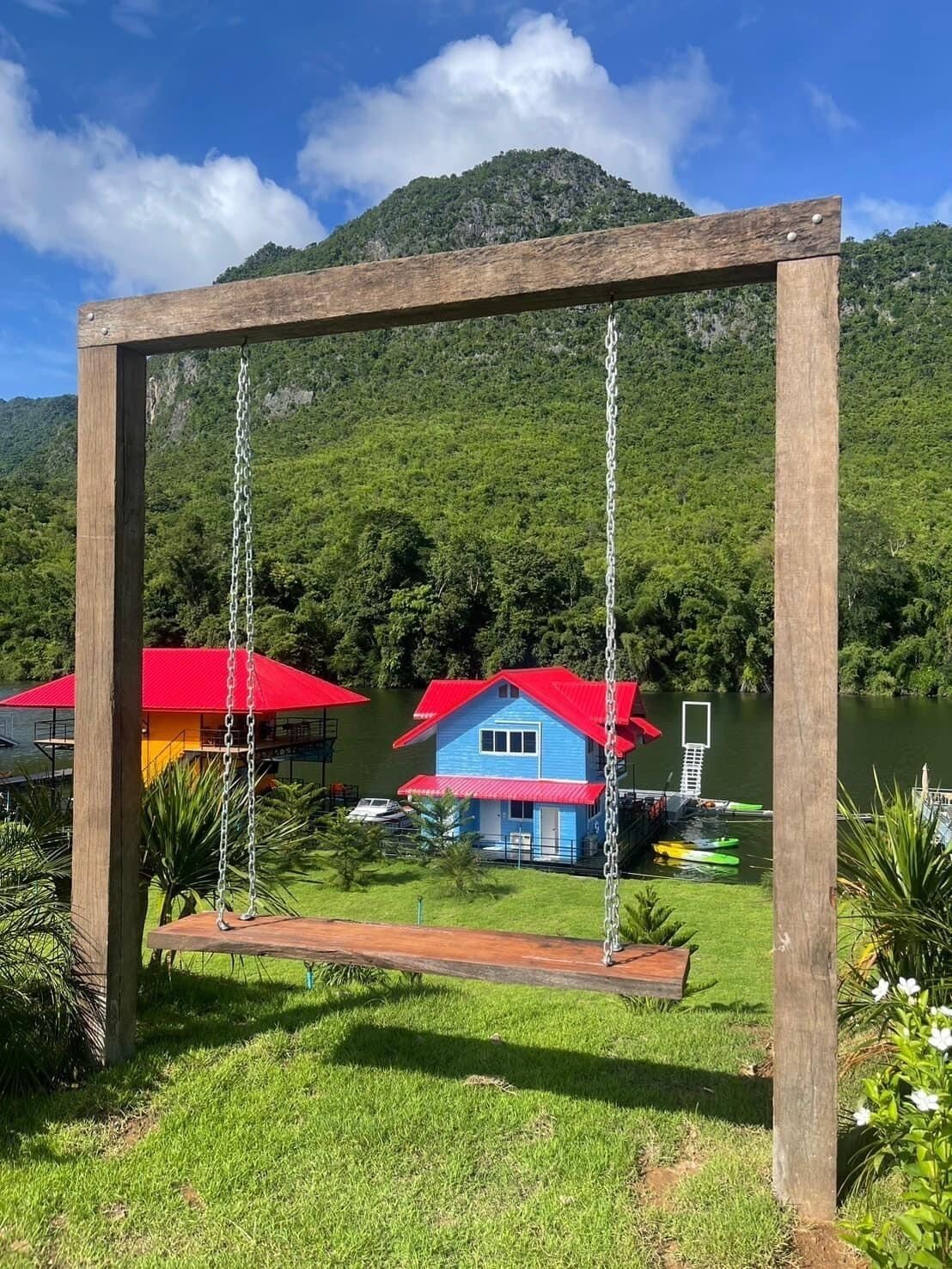 Un ensemble de balançoires en bois, installé dans un paysage verdoyant et luxuriant, avec un lac et une montagne en arrière-plan.