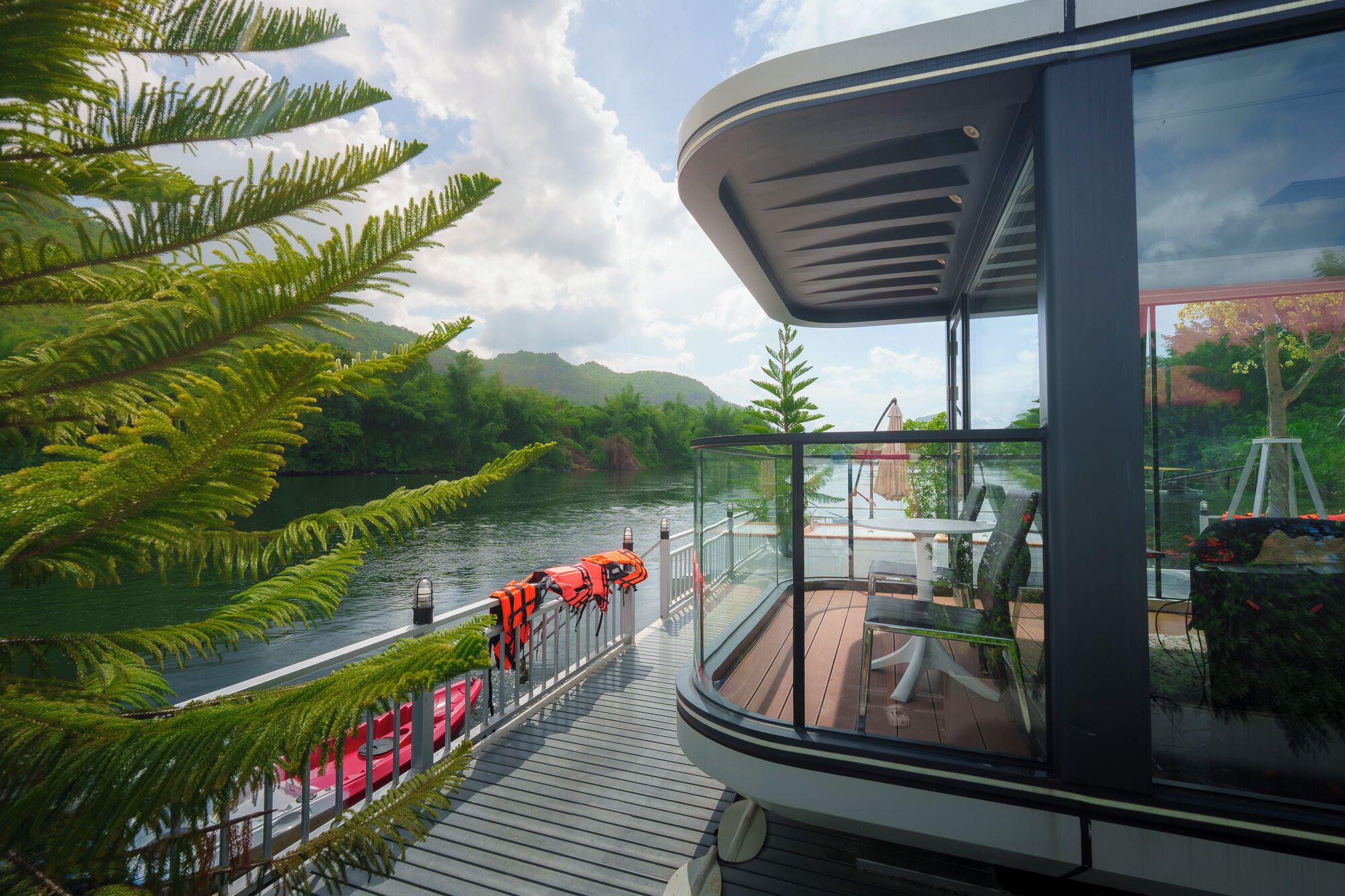 A glass-enclosed balcony with a view of a river and surrounding greenery.