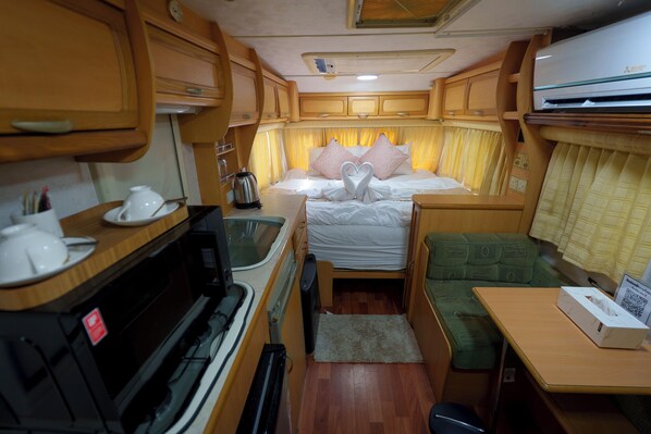 Interior compacto de una caravana con kitchenette, una cama decorada con cisnes y una pequeña zona de estar.
