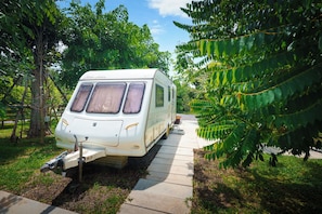 Un camping-car blanc est garé sur un chemin de béton, entouré de verdure.