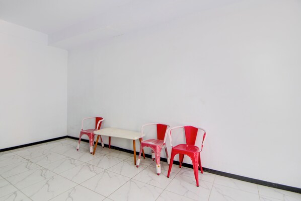 A room with a white tiled floor, a white table, and three red plastic chairs. - Hotel O Stasiun Tegal Near Alun-Alun  Formerly Ameera Guest House (Tegal)