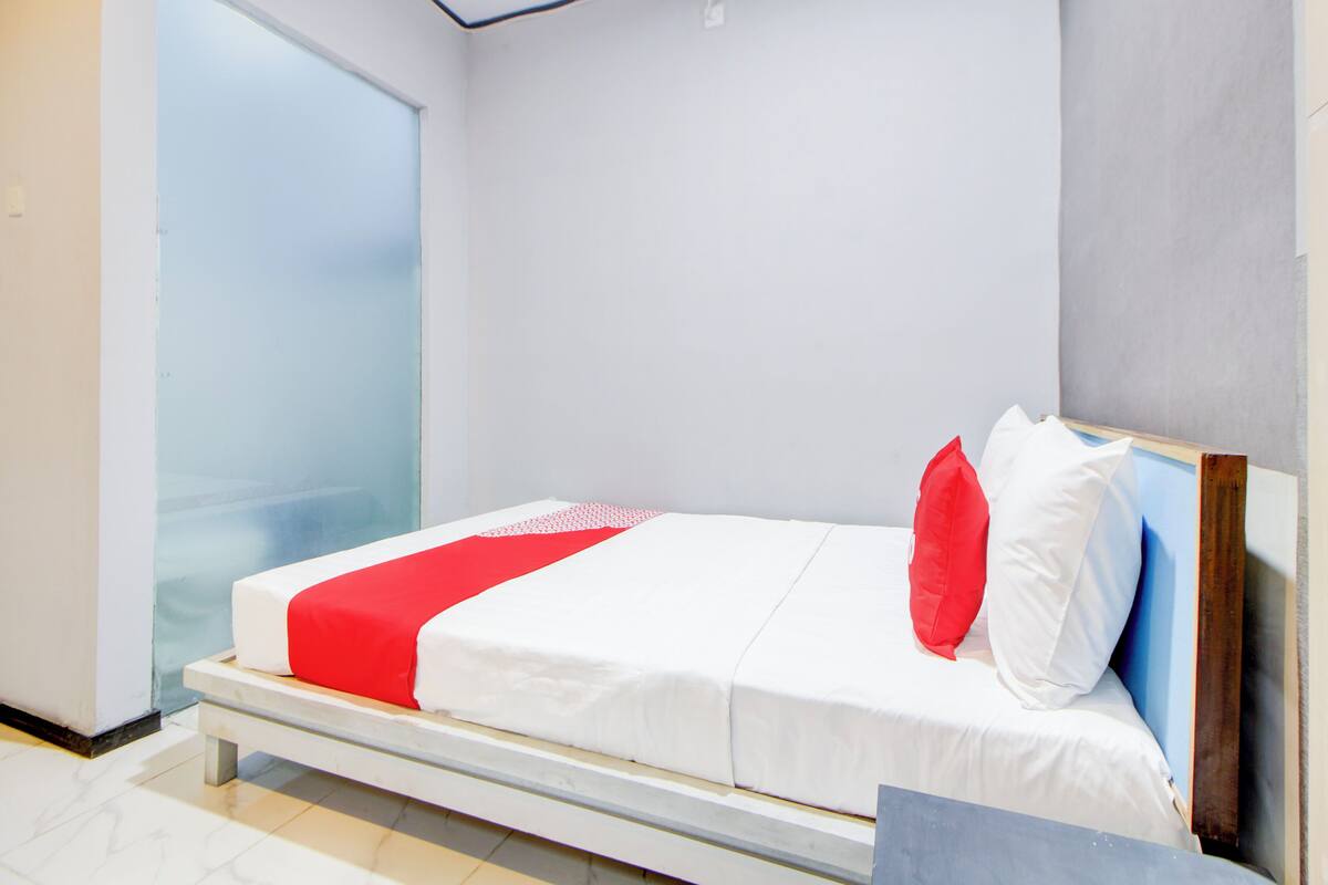 A modern hotel room with a bed, a red and white bedspread, and a large window.