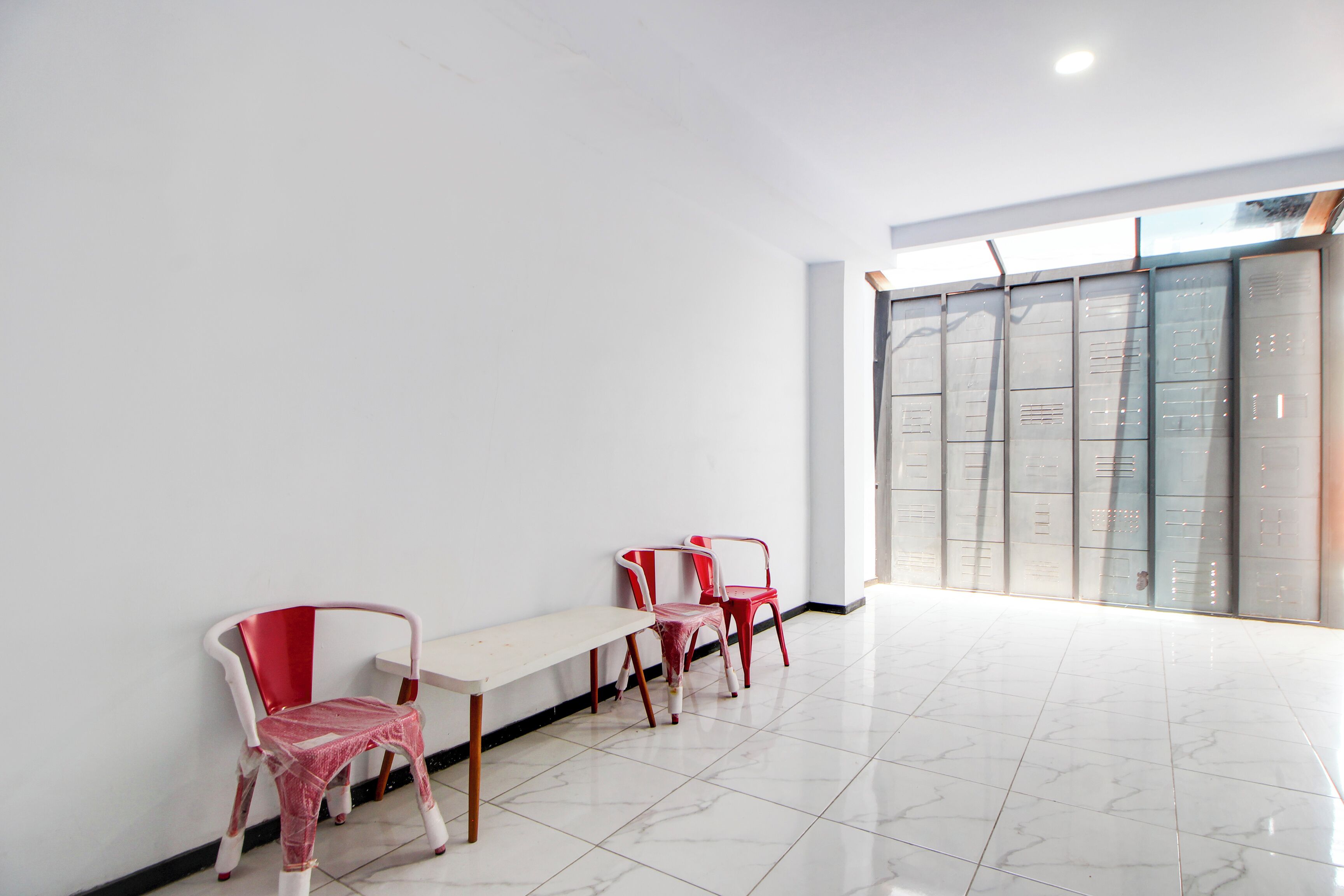 A room with a white wall, a bench, and three red chairs.
