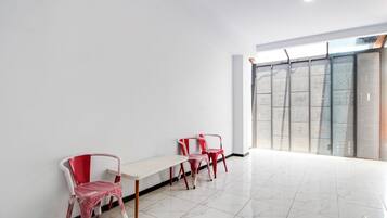 A room with a white wall, a bench, and three red chairs.