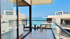 Un balcon avec vue sur la mer, une porte vitrée et une petite table avec des chaises.