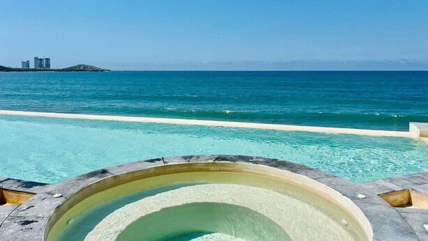 On peut clairement voir une piscine, avec une vue sur l’océan et une île lointaine parsemée de bâtiments.