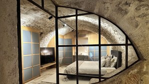 A rustic stone-walled room with a bed, a desk, and a television.