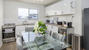 Een moderne keuken met witte kasten, roestvrijstalen apparatuur en een glazen eettafel met een bloemenvaas.