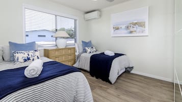 Une chambre d’hôtel avec deux lits, une fenêtre avec des stores, une commode en bois, un climatiseur fixé au mur et un tableau encadré accroché au mur.