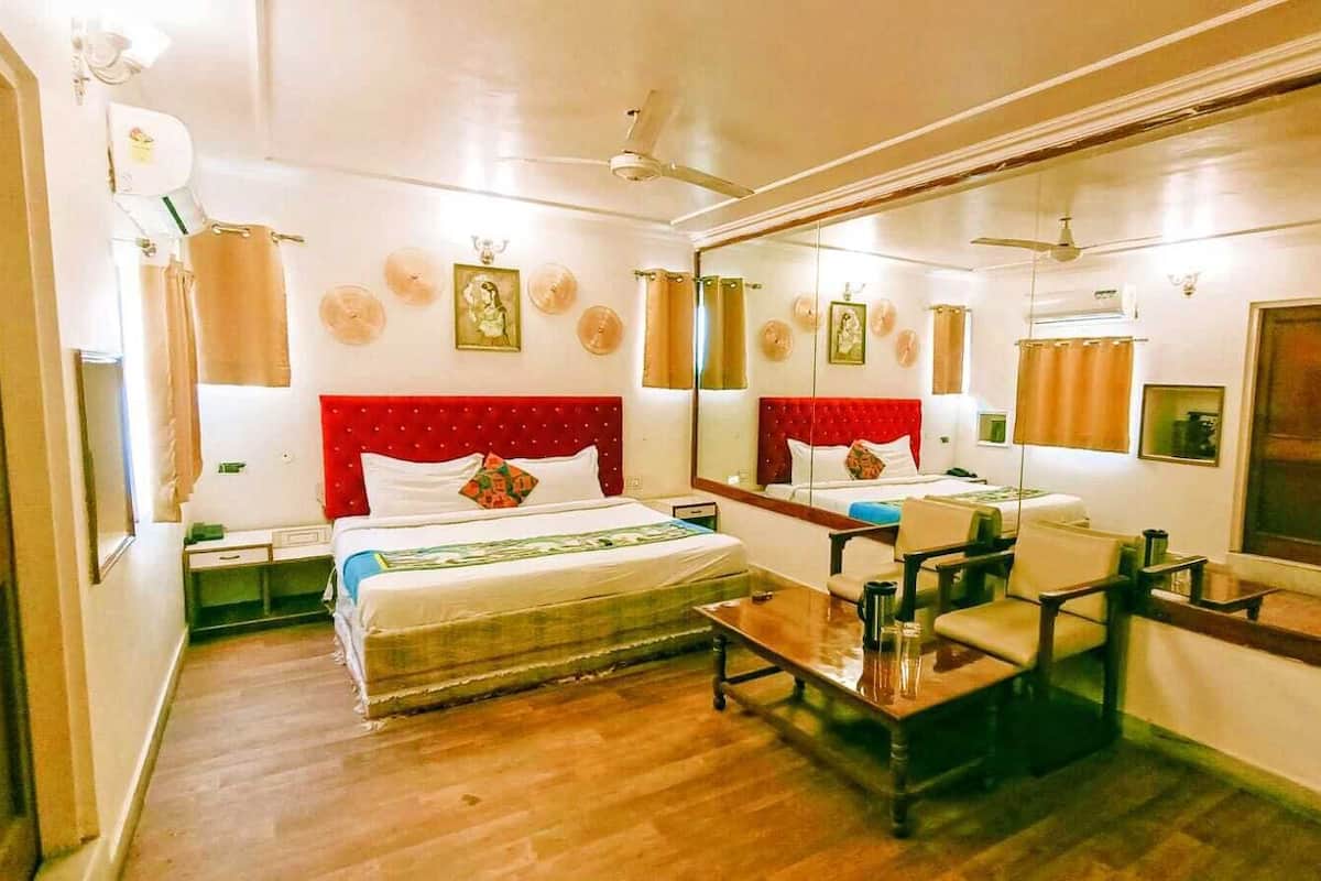 A hotel room with a large bed, a desk, a chair, a mirror, and a ceiling fan.