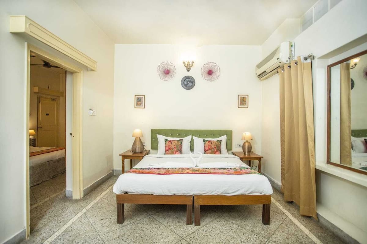 A hotel room with a wooden bed, two bedside tables with lamps, a green headboard, and a large mirror on the wall.
