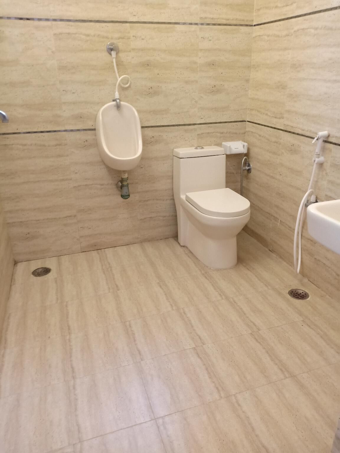 Ein kleines Badezimmer mit Fliesen, Toilette, Urinal und Dusche.