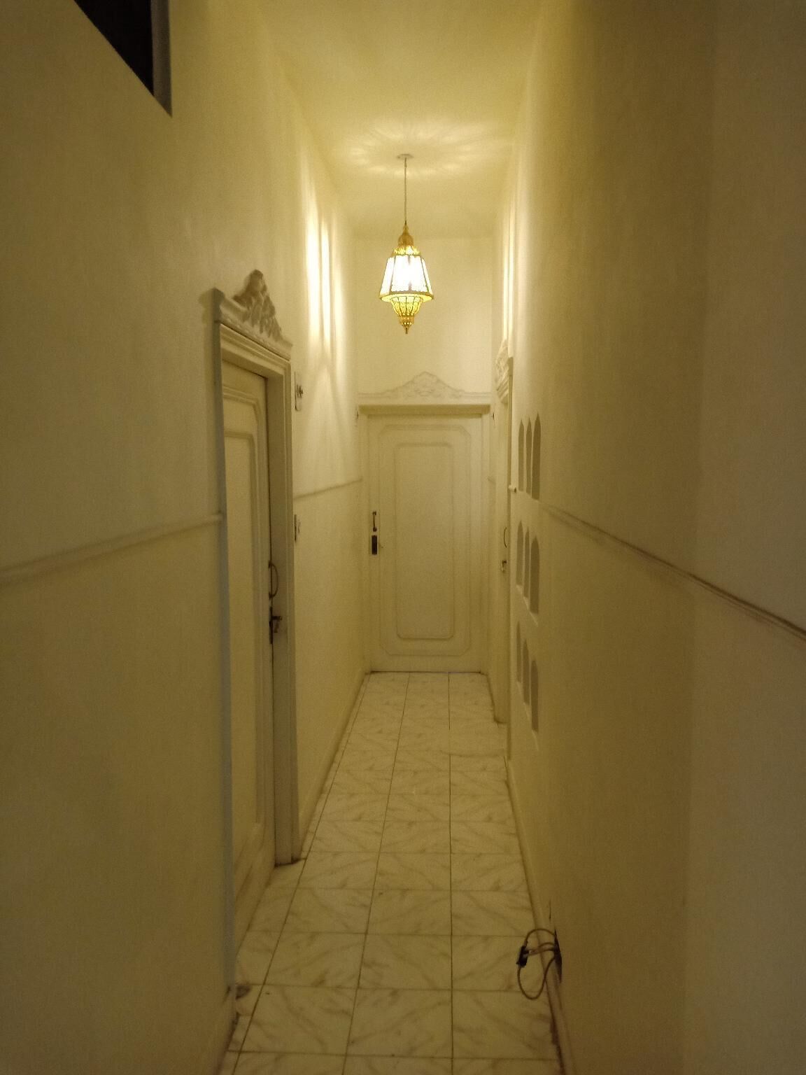 A narrow hallway with a door on the left and a light fixture above.