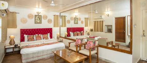 Habitación de hotel con una cama grande, zona de estar con una mesa y un espejo grande que refleja la habitación.