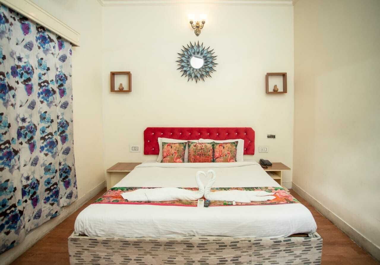 A hotel room with a bed, a red headboard, two nightstands, a wall-mounted mirror, and a floral curtain.