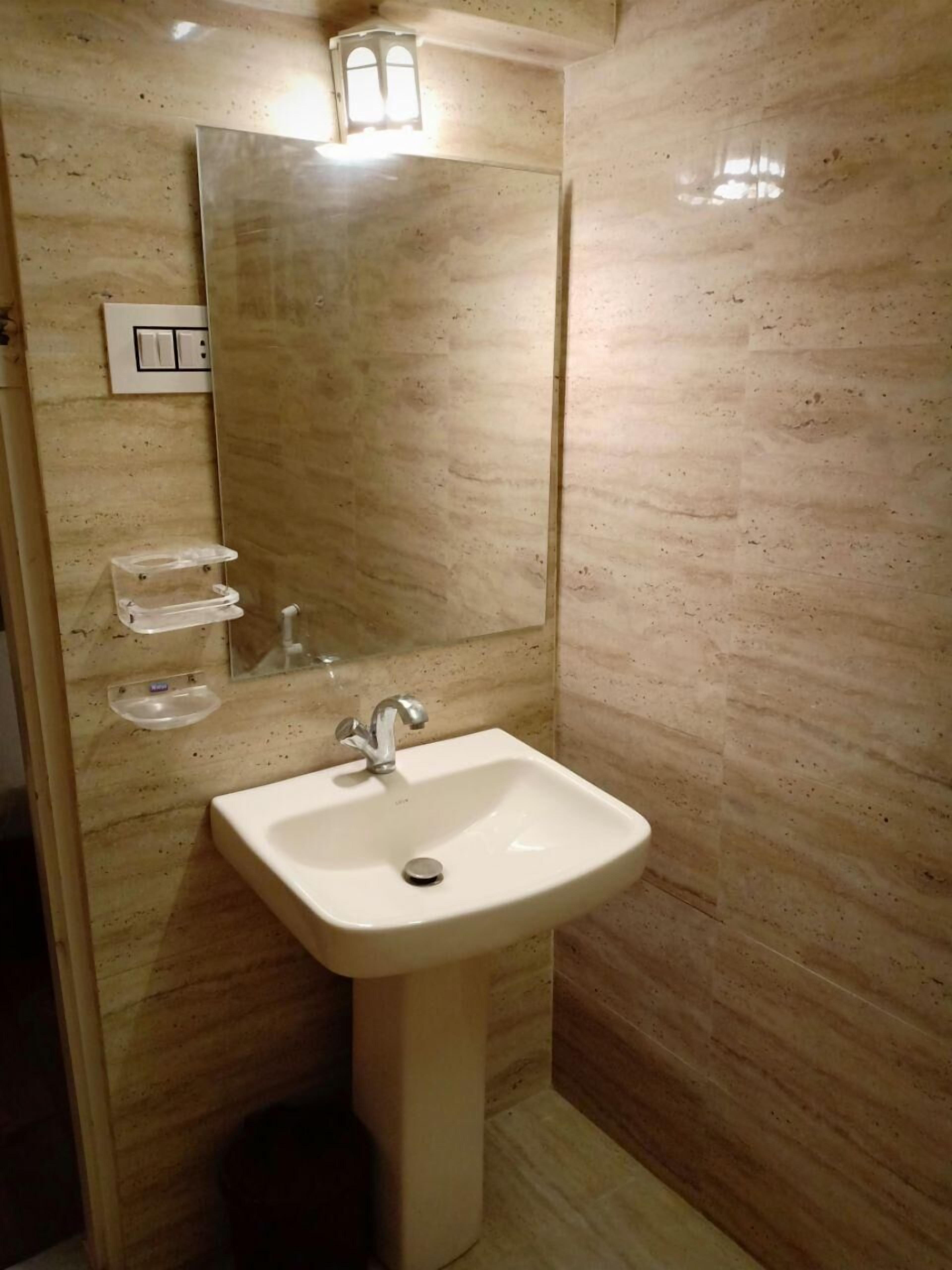 Casa de banho com lavatório assentado, espelho e candeeiro fixo na parede.
