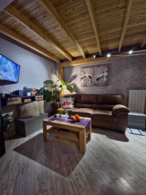 Un salon moderne avec un plafond en bois, un canapé en cuir marron, une table basse en bois sur laquelle sont disposés des fruits, un téléviseur et un tableau accroché au mur.