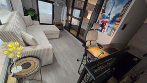 Un salon moderne comprenant un canapé, une table d’appoint avec un vase de fleurs, un bureau avec une chaise et une grande fenêtre offrant une vue sur la Tour Eiffel.