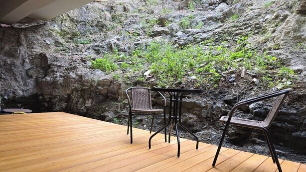 Une terrasse en bois avec deux fauteuils en osier et une petite table, le tout installé devant un décor rocheux.