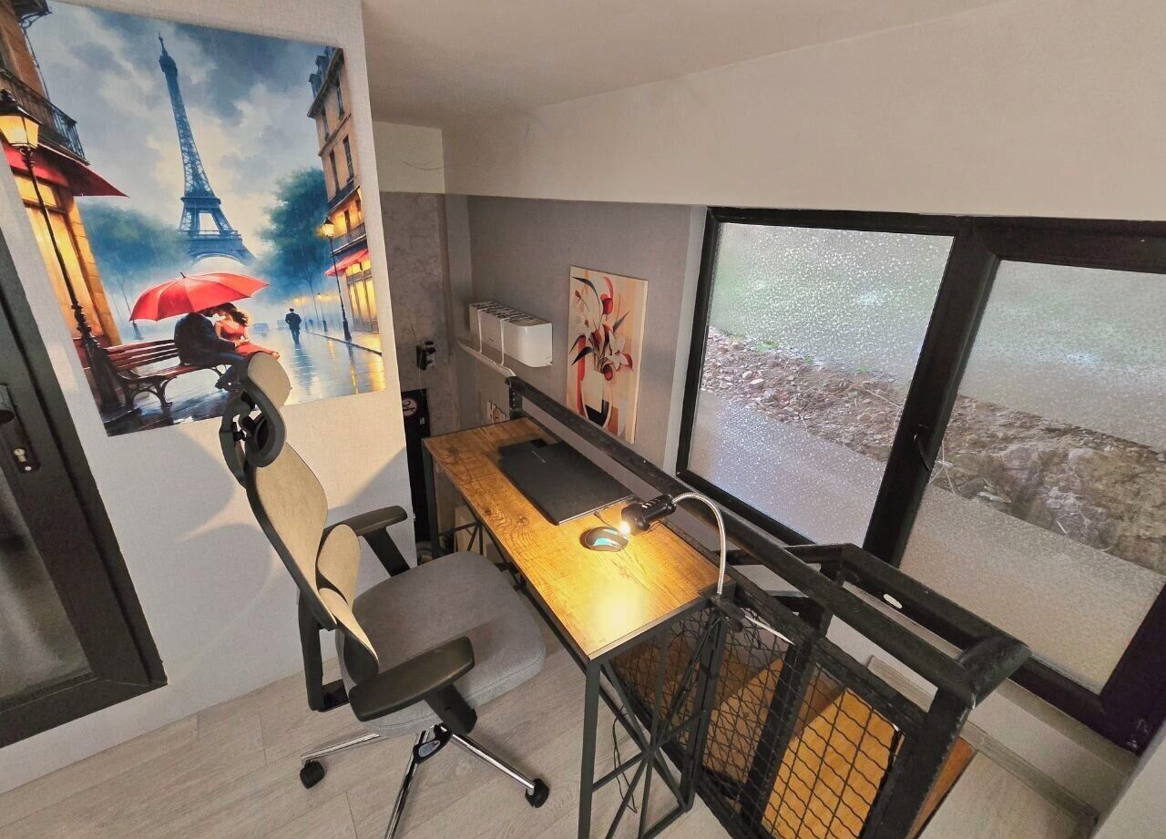 Een kamer met een bureau, stoel en een groot raam met uitzicht op de stad.