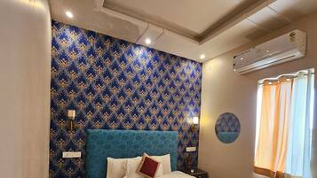 A hotel room with a large bed, a blue patterned wall, an air conditioning unit, and a window with curtains.